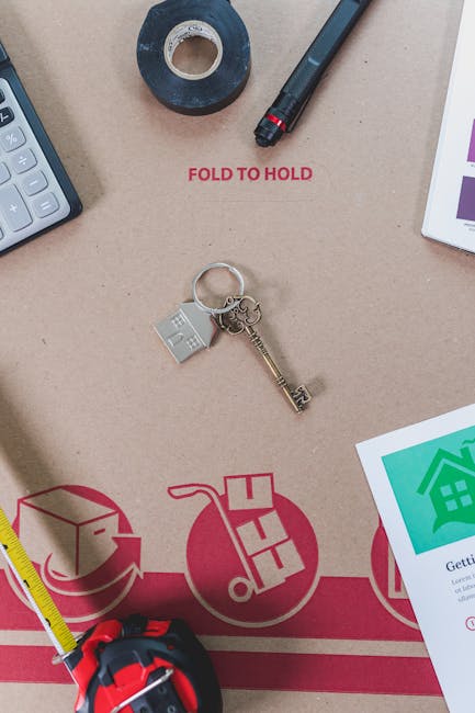 Close-up image showing a cardboard moving box with printed red and green symbols related to house relocation and packing, placed on a beige surface. The box features a red circular icon with a house a
